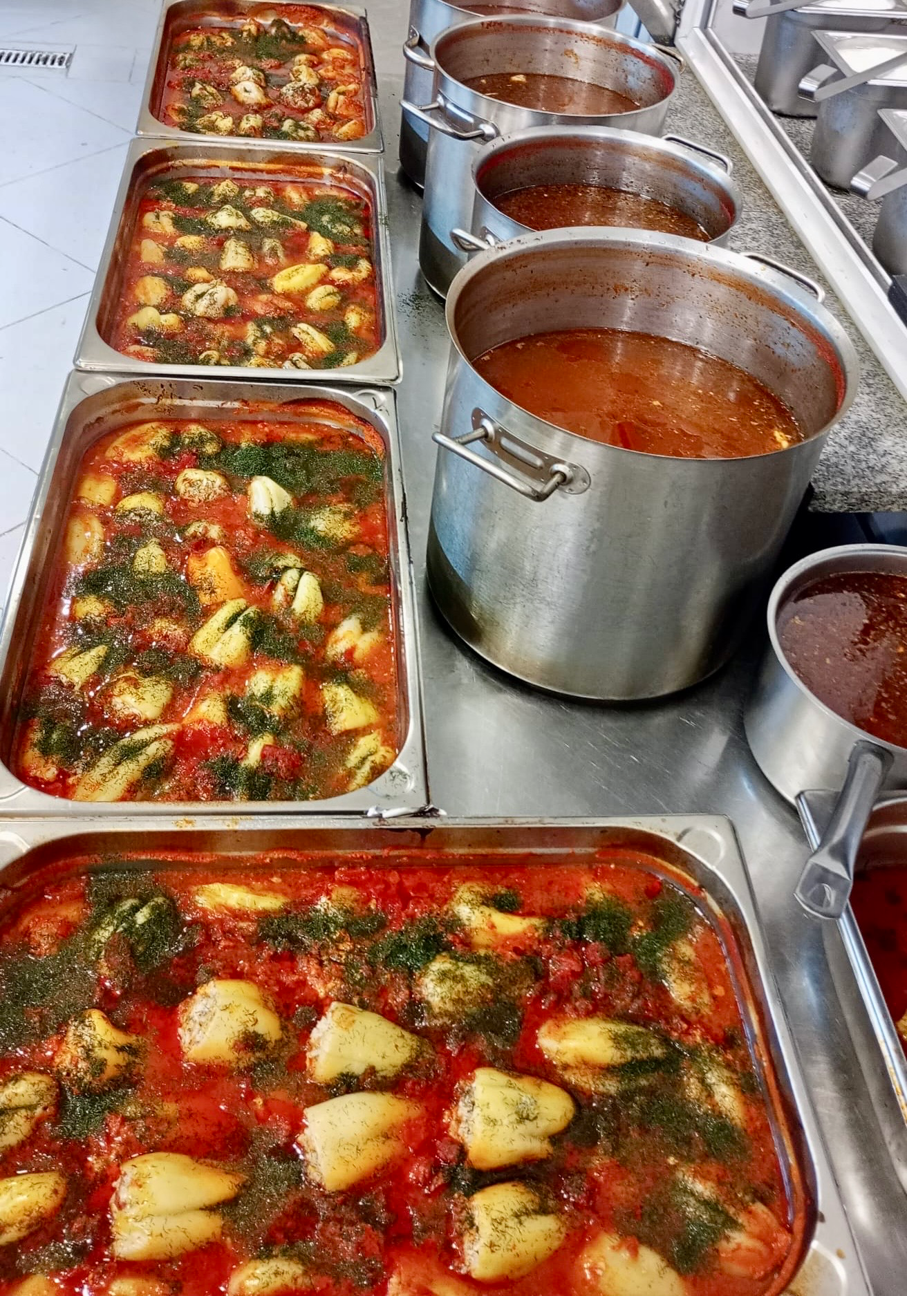 Tăvi inox cu găluște în sos de roșii și ierburi aromate, pregătite în cantități mari într-o bucătărie profesională de centru de îngrijire seniori din România