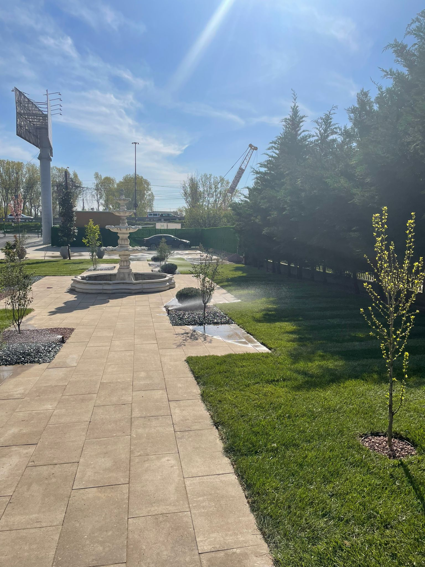 Gradina cu fantana arteziana in centru, aleei pavate, spatii verzi ingrijite si copaci tineri intr-un centru de ingrijire pentru seniori