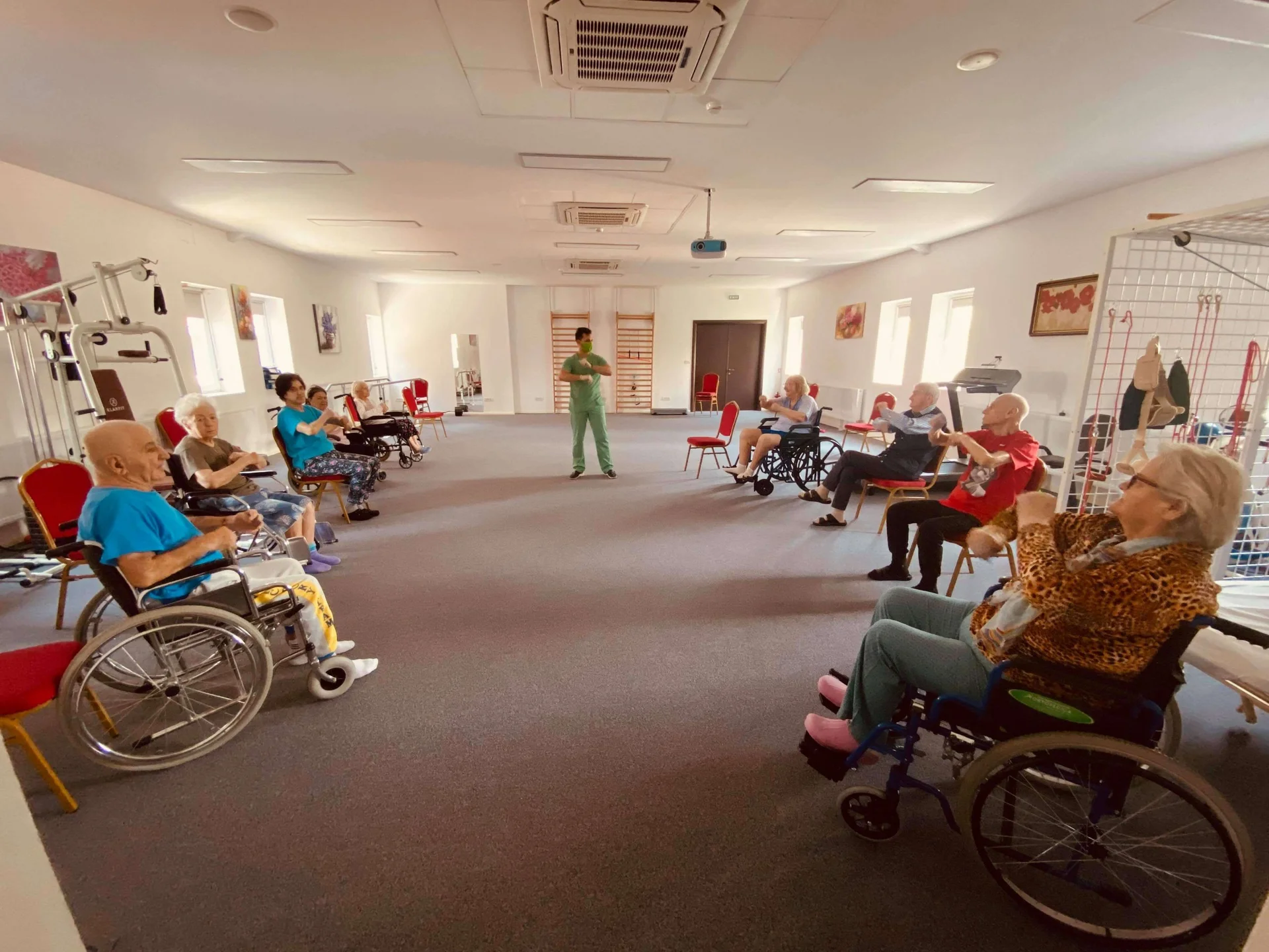 Sala de kinetoterapie cu seniori in scaune cu rotile participand la sedinta de recuperare sub supravegherea kinetoterapeut