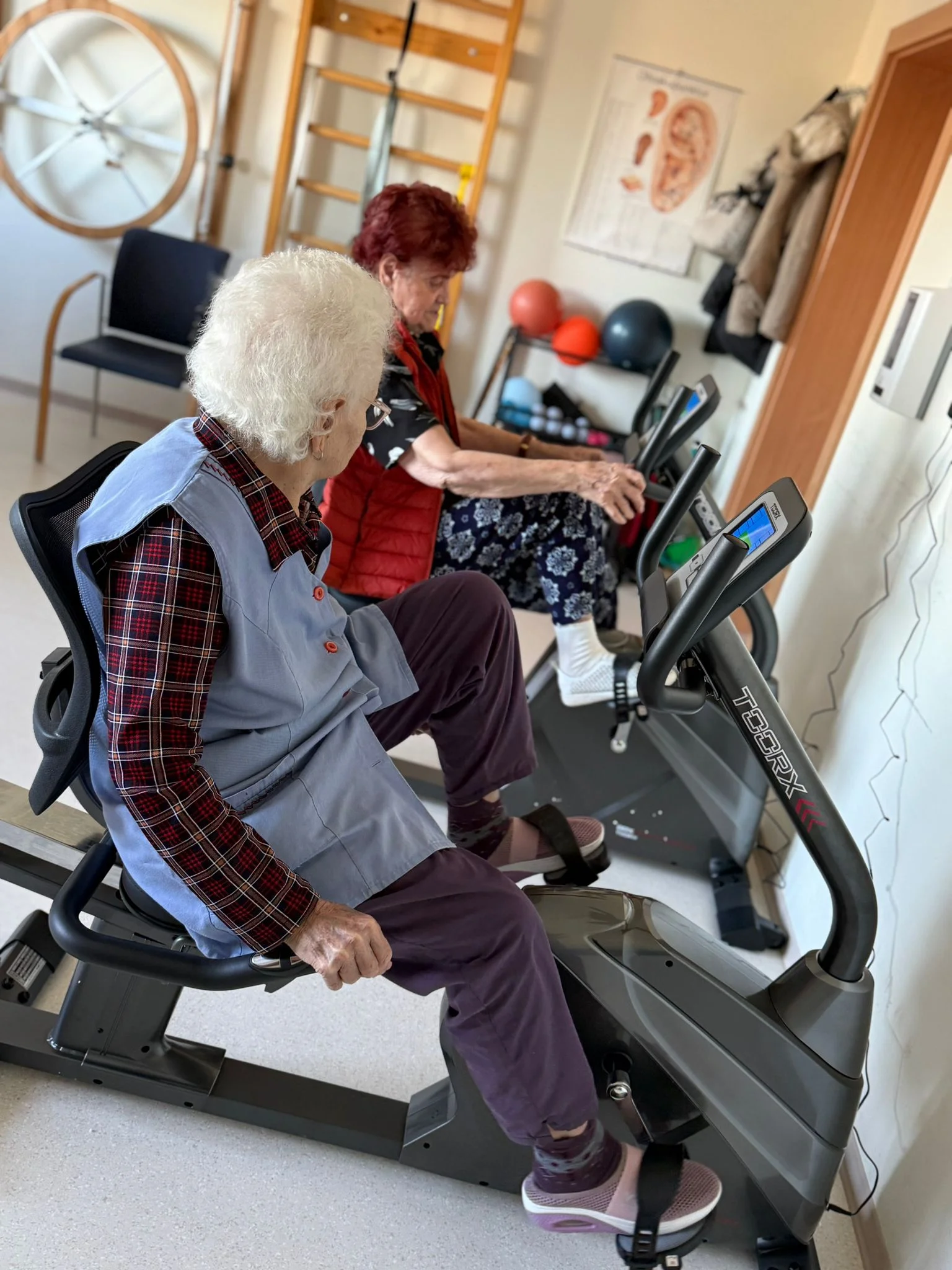 Doi seniori fac exercitii de kinetoterapie pe biciclete de recuperare medicala intr-o sala specializata de recuperare